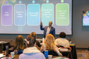 Instructor presenting biomagnetism concepts to participants during a Dr. Garcia Biomagnetism training seminar, with a visual slide explaining different muscle testing methods.