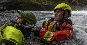 ICE-SAR rescue team members conducting a water rescue in a fast-moving river, wearing protective helmets and gear, with a Luminox watch visible on the rescuer’s wrist during a rescue training operation in harsh conditions.