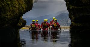 ICE-SAR rescue team wading through cold water in a remote Icelandic landscape, wearing protective helmets and rescue gear while advancing toward a rescue operation.