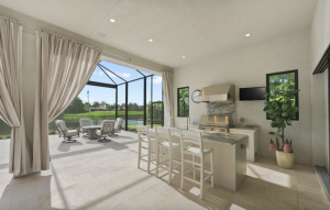 West-facing luxury lanai with wood ceiling, fireplace, outdoor kitchen, pool and spa overlooking the golf course and water at sunset.