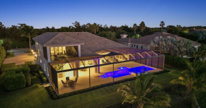 A view of the rear exterior at dusk featuring a large screened lanai, illuminated pool and spa, and landscaped backyard.