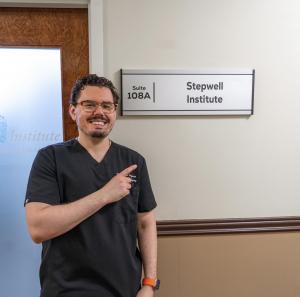 Dr. Yakov Groysman, podiatrist at Stepwell Institute in Manalapan, NJ, standing outside his office and pointing to the Stepwell Institute sign