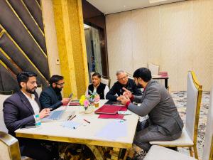 Mr. Sidharth Dhingra and Mega Realty Max team seated around a table in a formal meeting with clients, discussing property opportunities in an upscale conference room with gold-accented interiors.