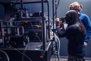 Two people around a microscope, one of them looking into the lens