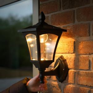 Wall-mounted outdoor lantern glowing on a brick house exterior at dusk