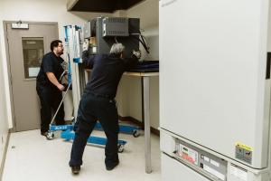 Two NOR-CAL Moving Services movers using lifting equipment to move microwave oven in commercial kitchen