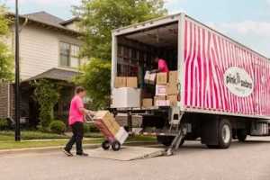 Pink Zebra Moving employee in pink shirt loading boxes onto distinctive pink and white striped moving truck