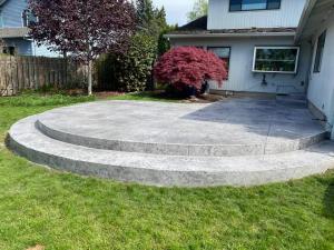 Custom curved concrete patio with tiered steps, finished with decorative stamped concrete for a modern backyard outdoor living space.
