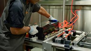 A technician in a grey LiThink uniform positions a black 25.6V 100Ah LiFePO4 battery on an industrial testing rig featuring red pneumatic hoses for quality control and mechanical stability testing.
