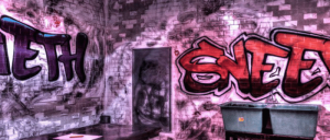 Interior of a graffiti-covered room featuring the words "SNEET" and "TEETH" on the walls, with a grey container in the corner.
