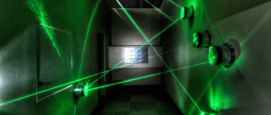 A hallway filled with green laser beams projected from circular devices against the walls, creating a maze-like effect.