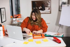Marketing strategist, Kristina Hernandez, is organizing sticky notes, notebooks, and campaign planning materials at a desk during a Creative Repute planning session.