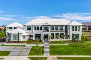 A high-end residential property featuring modern white architecture and professional landscaping under a clear blue sky.