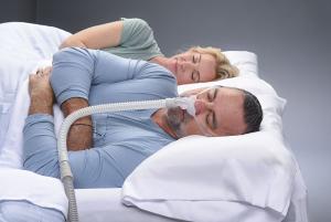 Middle aged male wearing the REMSleep DeltaWave mask while sleeping next to his wife.