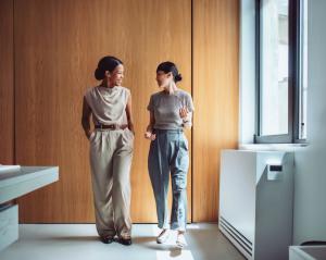 Two professional women having a relaxed conversation while walking through a modern office space.
