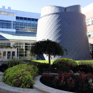 Modern building with a distinctive diamond-patterned gray structure surrounded by lush greenery and colorful flower beds.
