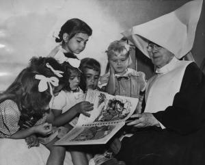 Black-and-white photo of a religious sister reading a book to several young children at Maryvale in Los Angeles County