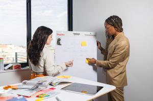 Two strategists review a website flow diagram on a whiteboard, illustrating early digital planning and brand infrastructure development for businesses preparing for increased demand and attention during large-scale global events.