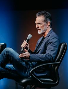 Tom Mueller, CEO of Impulse Space, speaking into a microphone during a fireside chat at SmallSat Symposium.