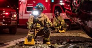 Firefighters at a nighttime road incident deploy a Peli 9730 Remote Area Lighting System to illuminate an overturned vehicle, with emergency vehicles in the background.