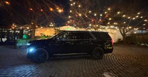 A black luxury SUV parked on a cobblestone driveway at night in front of a building with decorative string lights.
