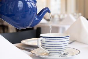 A close-up of tea being poured from a blue ceramic teapot into a striped teacup on a white tablecloth, highlighting the ritual and elegance of traditional tea service at The London Tea Room.