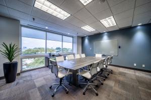 Conference room with white leather chairs, grey scale table, windows with a view of the neighborhood.