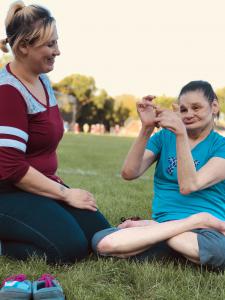 Direct Support Professional Jade sits in the grass with Sheila who loves being outside in the sun