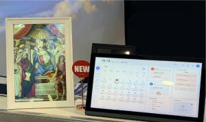 A real-life photo of the FotoCube AI Calendar device on display at CES 2026, showing the actual hardware texture, the vibrant 15-inch display, and a user interacting with the proactive AI scheduling feature.