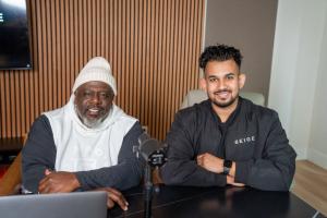 Kawser Khan and Cedric the Entertainer seated at podcast desk in Beige AI studio
