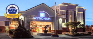 Wyndham hotel exterior with illuminated sign; a fountain and landscaped trees in front. Certified Autism Center logo displayed.