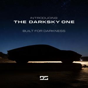 Side view of a black concept car parked on a desert road at night beneath a starry sky.