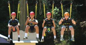 Four campers wearing helmets and harnesses sit in suspended seats during a ropes-course activity at Mt. Gilead Bible Camp and Conference Center in Sebastopol, California.