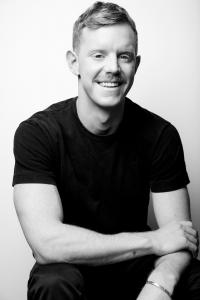 This is a black and white portrait photograph of George McGraw. He is seated, smiling at the camera with one arm crossed over the other.