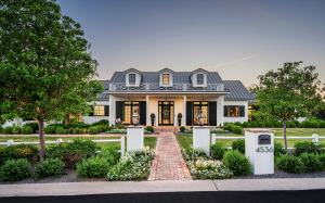 Exterior view of a luxury $6.75M Southern-inspired modern estate in Arcadia, Phoenix, showing white brick, a large covered front porch, and Camelback Mountain in the background under a clear blue sky