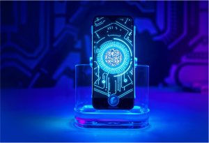 A smartphone displayed on a transparent acrylic stand, featuring a futuristic QR code interface on screen. The QR code is centered within glowing cyan concentric circles and surrounded by circuit board-style digital graphics. The scene is dramatically lit