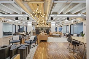 Image of the open coworking space at Strive Nashville. Photo shows golden brown wooden floors, modern grey and brown furniture, high industrial ceilings and sleek lighting fixtures