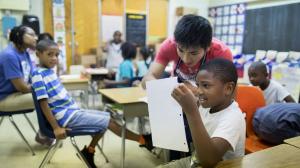 Educator assisting children in a classroom while students interact and participate in learning activities.