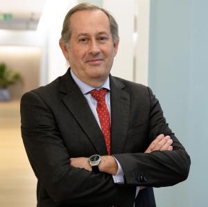 Pedro Rodríguez, wearing a dark suit and red tie, stands with arms crossed in a modern office corridor. He is the Director of Strategic Development and Sustainability at Aqualia.