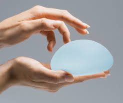 Close-up of two hands gently holding a smooth, translucent blue silicone breast implant against a neutral gray background.