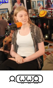 Vivian Jenna Wilson (21), long blond hair, smiles beside a dog. She sits at a streamer mic, right hand on left wrist. Below, her Toki Pona name (jan Wiwijan)  appears: person glyph + long oval cartouche with W +2 tallies, W +2 tallies, person +3 tallies.