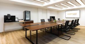A modern boardroom at Courtyard by Marriott Phuket Patong Beach Resort featuring a long wooden meeting table, ergonomic chairs, built‑in presentation screen, and a refreshment corner with coffee and tea facilities—ideal for executive meetings, small corpo