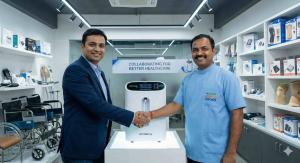 A corporate executive and a Healthy Jeena Sikho representative shaking hands warmly inside a modern medical equipment showroom. They stand beside a sleek OXYMED oxygen concentrator displayed on a lit pedestal. The background features a clean retail enviro