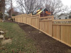 Custom wood privacy fence installed on a sloped residential yard with staggered panels following the landscape.
