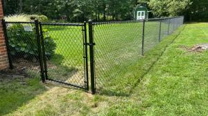 Black chain link fence installed along a residential backyard property line with a gate near a brick home.