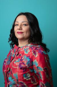 Portrait of Avv. Dipl.-Jur. Dominique Calcò Labbruzzo in a red patterned jacket, photographed against a turquoise background.