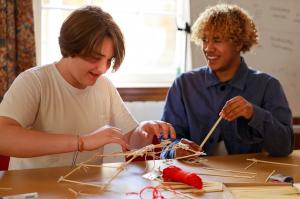 Two students collaboratively building a structure with wooden sticks and string during a class at Immerse's Oxford Program