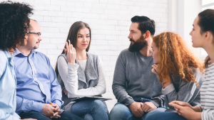 Image of men and women sitting in a half-circle at at 12-step meeting