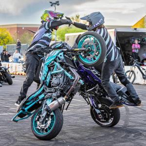 Two motorcycle riders balance motorcycles upright during a stunt performance