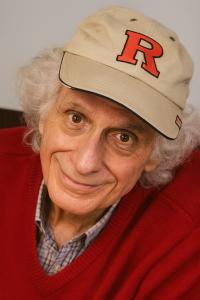 Portrait of author Calvin Barry Schwartz wearing a Rutgers cap and red sweater, looking directly at the camera with a warm expression.